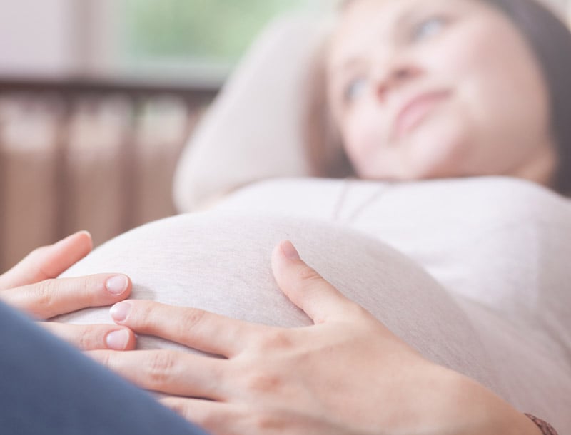 Schwangere Frau liegt auf der Couch und fasst sich an den Bauch